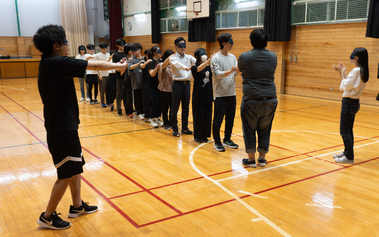 参加者が縦一列になりアイマスクをして前の人の肩を掴んでいる状況の画像